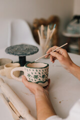 Design earthenware cup with a traditional pattern. Artist is making decoration on the clay ceramic mug after oven firing.