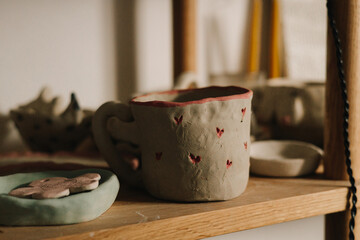 Shelf with handmade clay cups and plates in the pottery studio. Creating ceramics ware with own hands.