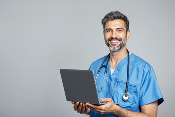 Smiling male doctor in blue scrubs with a stethoscope using a laptop.