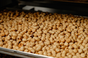 Freshly roasted nuts spread across a tray in a bustling market, highlighting the artisanal craft of nut roasting during early morning hours