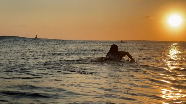 Long haired young caucasian male surfer paddling on a surfboard in the transparent water of the Indian Ocean. The golden hours time. Bali island. Indonesia. Wide-angle slow motion video.