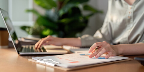 Financial analyst reviewing charts and data on clipboard while using laptop for calculations.