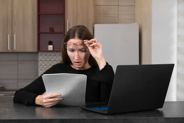Stunned woman working from home, raising her glasses while reading documents, displaying a shocked...