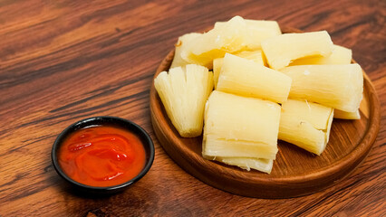 boiled cassava served on a wooden background. with spicy red chili sauce