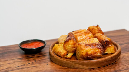 fried cassava served on a wooden background. with spicy red chili sauce