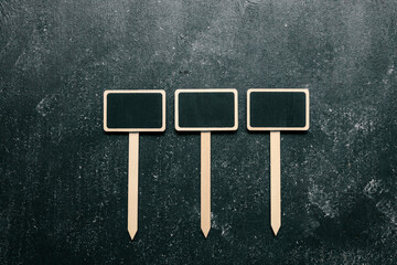 Three blank wooden chalkboard plant labels on a dark textured background. Minimalist gardening markers for organizing herbs, vegetables, and flowers. Space for customizable text or names