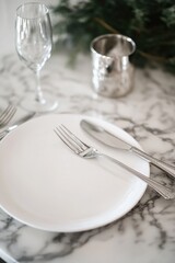 A refined table setting for two persons, including fine china plates, silverware, and wine glasses, all elegantly arranged on a marble tabletop. Decorated with holiday cheer.
