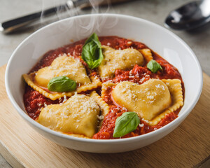 A steaming bowl of ravioli in rich tomato sauce, garnished with fresh basil and sprinkled with cheese, served on a wooden board.