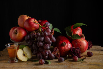 Still life with red apples, pomegranates and grapes on wooden table, black background, horizontal