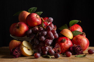 Still life with red apples, pomegranates, green leaves and grapes, black background, horizontal