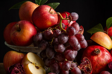 Close-up with red apples, pomegranates and grapes, black background, horizontal