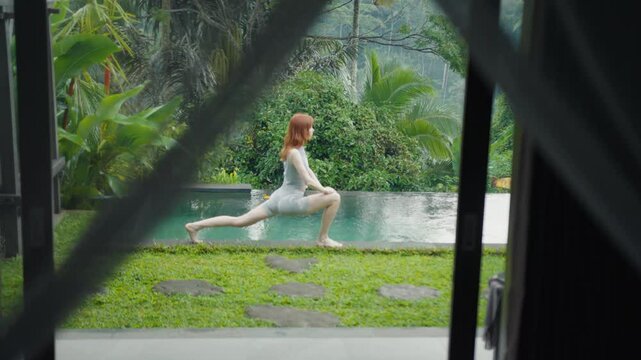 beautiful red-haire gitl doing stretching in the morning witho green jungle background on Bali