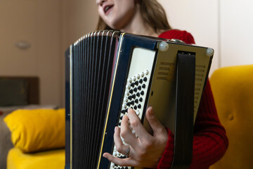 Young woman musician playing a striking black and gold accordion, singing with infectious enthusiasm and joy in a bright, inviting room filled with creativity and emotion