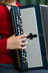 Musician wearing a red sweater skillfully plays a traditional accordion, her hands moving...