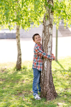 Happy boy hugging a tree in a green park on a sunny day.