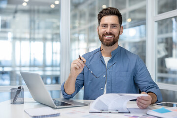 Portrait of successful financier at workplace, man smiling and looking at camera. Businessman...
