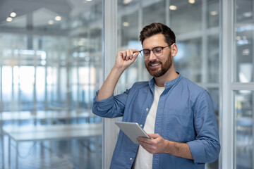 Young successful man with tablet computer inside office at workplace. Businessman reading online...