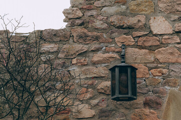 Historic stone wall with a vintage lantern and bare branches in a serene, overcast outdoor setting