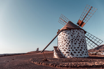 View of the old, typical windmills of Villaverde, Fuerteventura, Canary Islands, with their wooden blades. almost sunset, oblique light, golden hour. Past, vintage feeling.