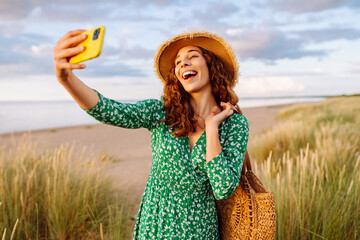 Young woman walking to the sea along the tall grass takes a selfie on her phone. Summer walks....