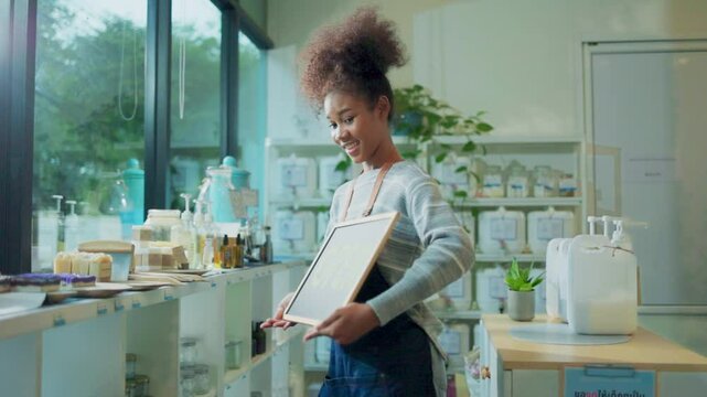 African young woman owner hold open sign at refill shop.