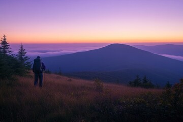 Obraz premium Hiker silhouetted against a vibrant sunrise over a mountain range and valley fog.