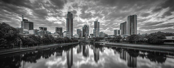 Fototapeta premium Monochrome cityscape reflected in calm water under dramatic clouds.
