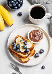 Toasted bread with chocolate cream, blueberries and banana on a plate on a light background