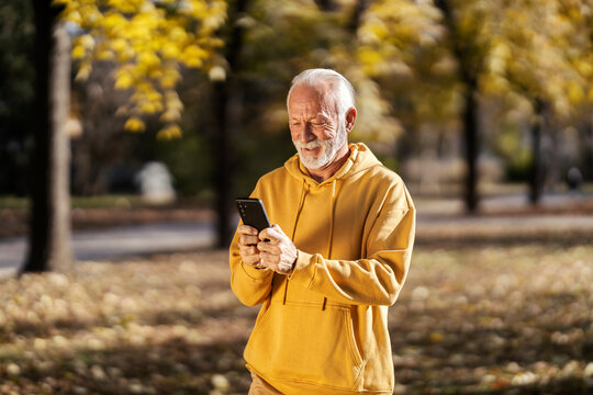 Fit senior athlete using fitness app on mobile phone and smiling at it during outdoor fitness.