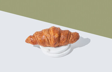 Fresh croissant on a marble stands on a green and white  background with shadow.
