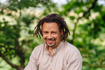 Bright portrait of a charismatic man with dreadlocks, captured outdoors in nature, radiating...