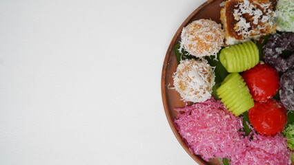 Various market snacks consisting of klepon, awug, jalabria, getuk, putu mayang and cikak are served on a wooden plate lined with banana leaves placed on a white base and background (isolated white).