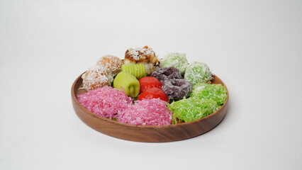 Various market snacks consisting of klepon, awug, jalabria, getuk, putu mayang and cikak are served on a wooden plate lined with banana leaves placed on a white base and background (isolated white).