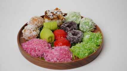 Various market snacks consisting of klepon, awug, jalabria, getuk, putu mayang and cikak are served on a wooden plate lined with banana leaves placed on a white base and background (isolated white).