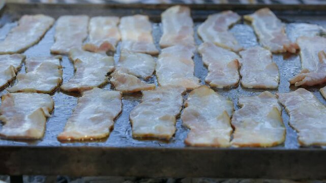 Stripe pattern as strips of bacon fry on large hot griddle outside