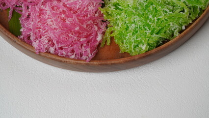 Various market snacks consisting of klepon, awug, jalabria, getuk, putu mayang and cikak are served on a wooden plate lined with banana leaves placed on a white base and background (isolated white).