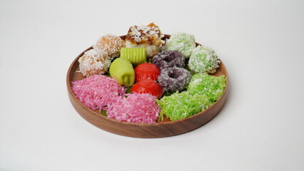 Various market snacks consisting of klepon, awug, jalabria, getuk, putu mayang and cikak are served on a wooden plate lined with banana leaves placed on a white base and background (isolated white).