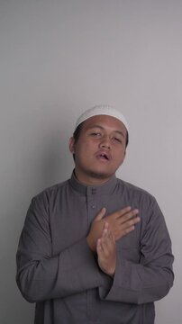 Southeast Asian Muslim man wearing grey robe makes greeting gesture then chats amiably with people around him