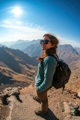 Naklejka premium Portrait of happy female tourist standing on top of mountain ridge with mountains in background. side view. looking back. fisheye lens