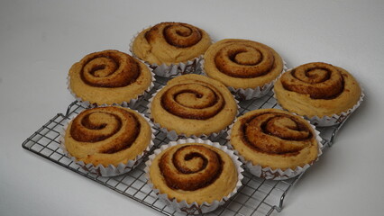 A collection of cinnamon rolls using paper cups and placed on a cooling rack with a white background (isolated white).