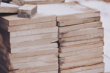 A neat stack of concrete slabs is arranged in an outdoor area, illuminated by the soft glow of morning sunlight, highlighting their smooth surfaces and rough edges, awaiting use
