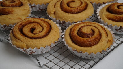 A collection of cinnamon rolls using paper cups and placed on a cooling rack with a white background (isolated white).