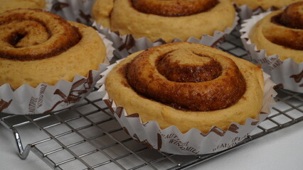 A collection of cinnamon rolls using paper cups and placed on a cooling rack with a white background (isolated white).