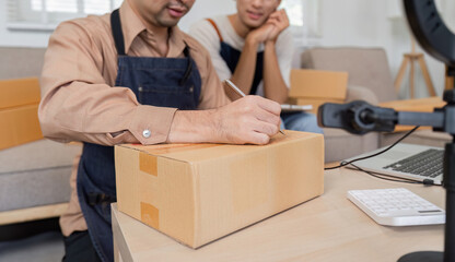 Focused online seller writing shipment details while another looks on, showcasing teamwork and...