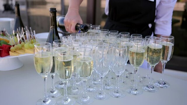 The waiter pours champagne into glasses at the reception of the event
