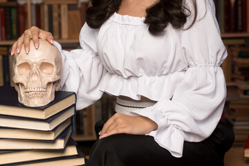 Female researcher in historical attire examines a human skull in a book-filled study. Concept of medical research, archaeology, and historical studies.