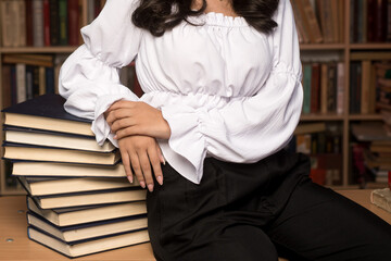 Fototapeta premium Close-up of a person sitting in a library, leaning on a pile of books. The image symbolizes study, reading, intellectual growth, and the pursuit of knowledge.