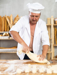 Man works in bakery as baker, kneads dough, works with flour.