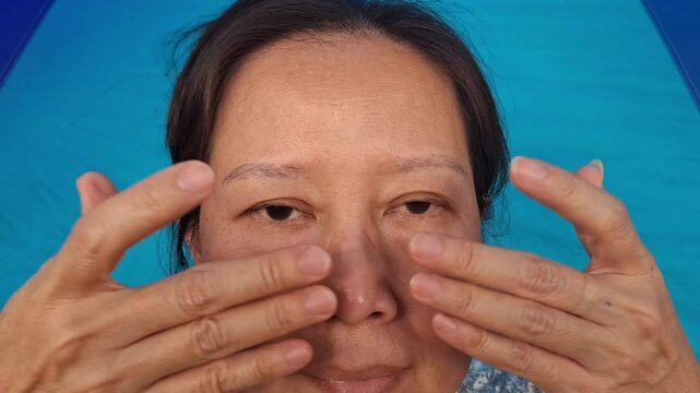 A woman uses her fingers to wipe away wrinkles on her face under the eyes.
