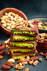 Dubai Chocolate bar with green kadayif and pistachio spread with pistachio nuts. Side view. On a dark stone background.